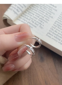 Macro detail of silver S925 bow-knot C-shaped earrings held in hand over a book