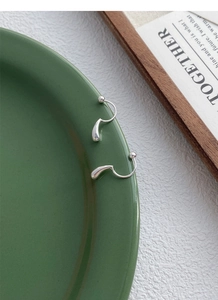 Macro detail of S999 sterling silver teardrop screw-back earrings on a green ceramic dish