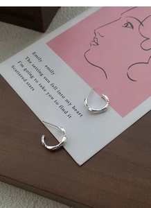Detailed macro view of S925 silver bamboo-style C-shaped hoop earrings on a wooden background
