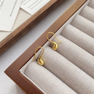 Eleganti orecchini a goccia d'oro in una scatola di legno con design a gancio minimale
