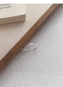Detail view of a minimalist S999 silver open fish ring on a textured paper background