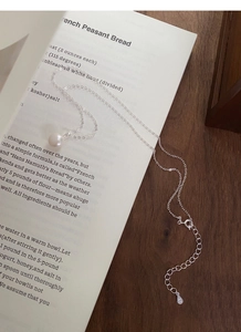 Gros plan sur collier en argent S999 avec perle d'eau douce sur un vieux livre ouvert