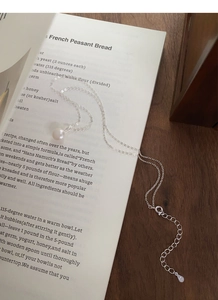 Détail d'une chaîne en argent S925 avec une perle d'eau douce posée sur un livre ouvert