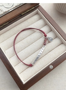 Detail of red braided rope bracelet with silver tube and Ping An engraved pendant
