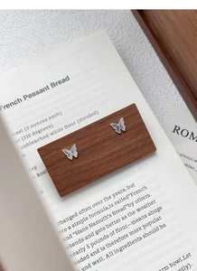 Détail de boucles d'oreilles papillon asymétriques en argent sur un support en bois foncé