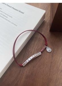 Detail of S999 silver tube red rope bracelet with Ping An pendant on a book