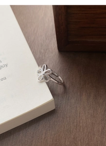 Detailed view of an S925 sterling silver hollow flower ring clipped on a white book page