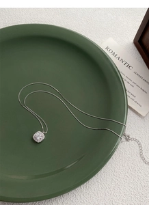 Detailed close-up of a cushion-cut silver necklace on a minimalist dark green tray