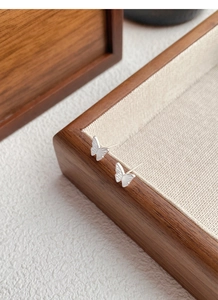 Détails macro des puces d'oreilles papillon en argent sur présentoir en bois et lin chic