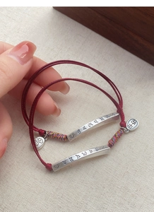 Macro detail of red woven bracelet with silver curved tube and Ping An pendant charm
