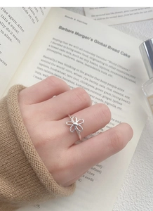 Detail of S925 sterling silver hollow flower ring worn on finger over an open book