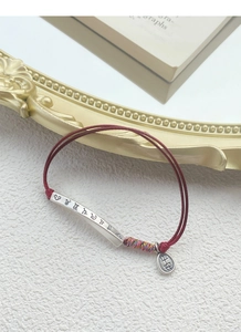 Close-up of S999 silver mantra tube and Ping An tag on a red braided bracelet