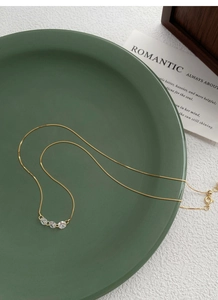 Détail du collier en argent S925 doré avec trois oxydes de zirconium sur plat vert
