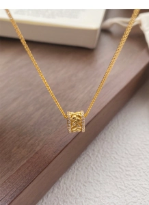 Détail du pendentif cylindre doré avec motifs de blé et petits diamants latéraux
