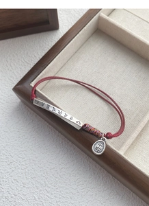 Detail of red braided bracelet with silver bar and 'Ping An' engraved charm