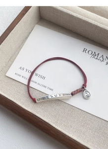 Detailed shot of red cord bracelet with silver curved bar and Ping An lucky charm