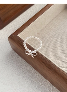 Close-up of S925 silver bow ring with white pearls on a rustic wooden tray display