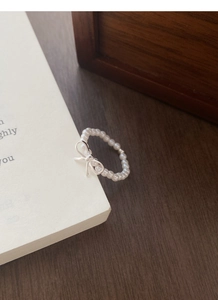 Detail of elegant pearl beaded ring with silver bow charm on a book background