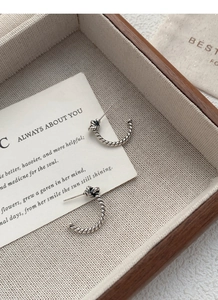 Macro shot of S925 sterling silver twisted rope knot earrings on a wooden display tray