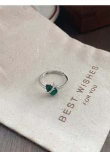 Detail of S925 silver gourd ring with green stones on a soft beige gift pouch