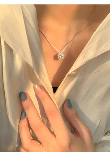Close-up of a square zircon pendant on a silver necklace worn by a model in soft light