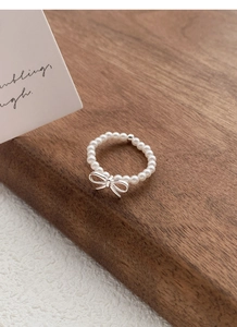 Detail of the elastic pearl ring featuring a silver bow pendant on a wooden stand