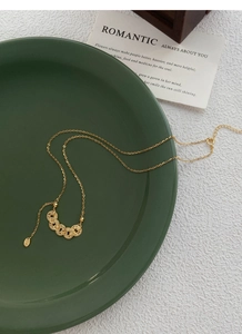 Detailed close-up of gold S925 sterling silver coin tassel necklace in a ceramic dish