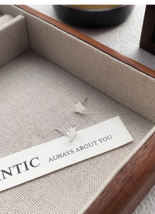 Detailed view of S999 sterling silver star stud earrings on a beige linen jewelry tray