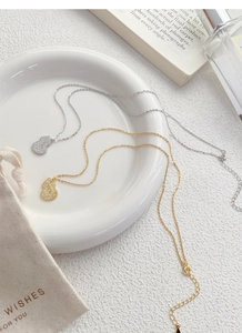 Detail view of gold and silver gourd pendants with hammered texture on a ceramic plate