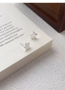 Detailed view of S999 silver star stud earrings with a textured crushed ice finish on a book
