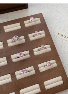 Detail view of pink zircon rings with silver metal bands on a wooden display tray