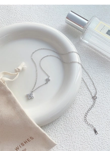 Detail of S999 sterling silver clover necklace with zircon pendants on white porcelain plate