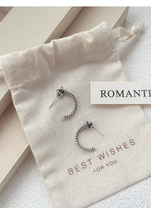 Detail view of knot-style twisted rope silver earrings on a beige fabric gift pouch