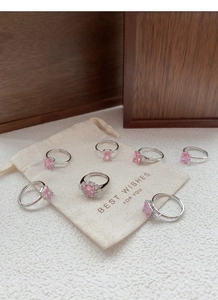Set of seven S925 silver rings with pink zircons on a beige pouch and textured tabletop