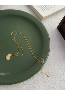 Detail of a golden S925 silver gourd pendant necklace on a green display plate