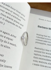 Macro shot of minimalist silver six-prong cubic zirconia ring placed on a book