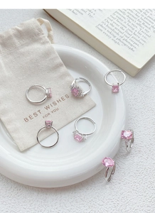 Detailed view of silver rings with pink zircons on a gift pouch and book background