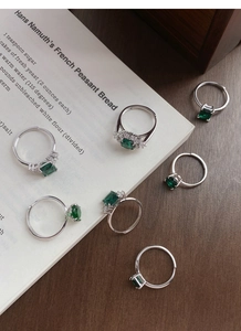 Detailed set of seven emerald green zircon rings in silver setting on vintage background