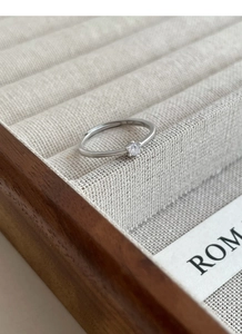 Detailed top view of a classic four-prong solitaire silver ring on a linen display tray