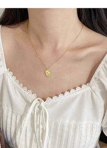 Detailed view of the gold-toned gourd pendant featuring a unique hammered texture on model
