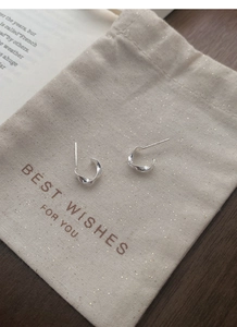 Detail of silver Mobius C-shaped earrings displayed on a gift pouch with a vintage book background
