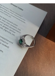 Detailed view of an emerald green gemstone ring on a book page with silver band