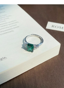 Macro detail of square emerald green zircon ring with sparkling side stones on a book