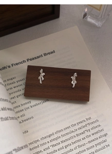 Close-up of S999 silver bow earrings with ribbon texture on a wooden stand