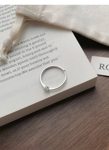 Detail of adjustable silver solitaire ring with zircon stone on open book background