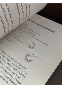 Detail of twisted S999 silver Mobius earrings placed on an open book with rustic wood background