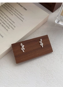 Detail of silver bow earrings on a wooden display with elegant lifestyle background