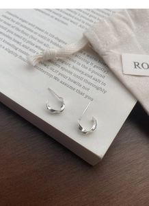 Detail of S999 sterling silver Mobius C-shaped earrings on a book page with a pouch