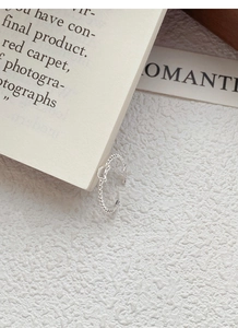 Detail of silver twisted band ring featuring a delicate heart charm on white aesthetic background