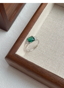 Detailed view of emerald-cut green gemstone ring with side zircons on a canvas background